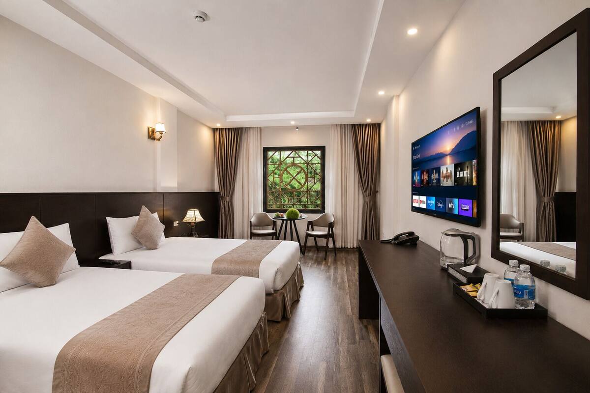A hotel room with two beds, a desk with a TV, a coffee maker, and a window with curtains.