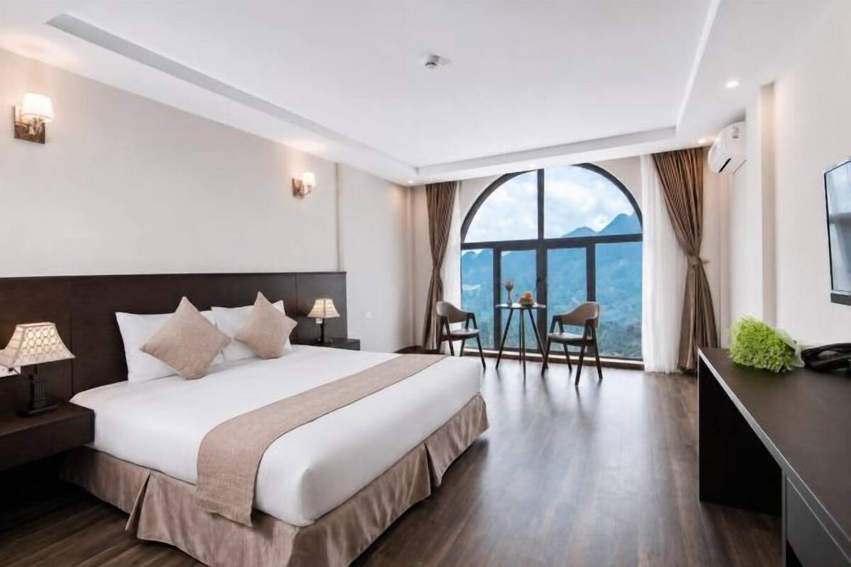 A hotel room with a large bed, a desk, a chair, and a view of the outdoors.
