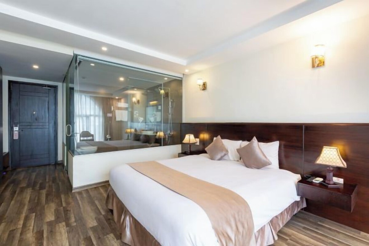 Habitación de hotel con una cama grande, mesitas de noche, un espejo y vistas al pasillo.