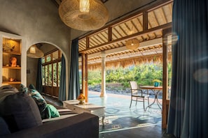 A room with a sofa, a table, and a view of greenery outside. - Darmada Eco Resort (Sidemen)