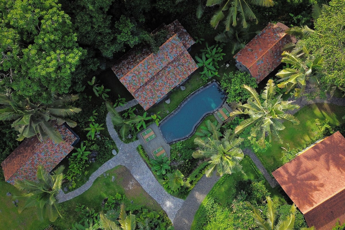 Vista aérea de un resort con varias construcciones, una piscina y exuberante vegetación tropical.