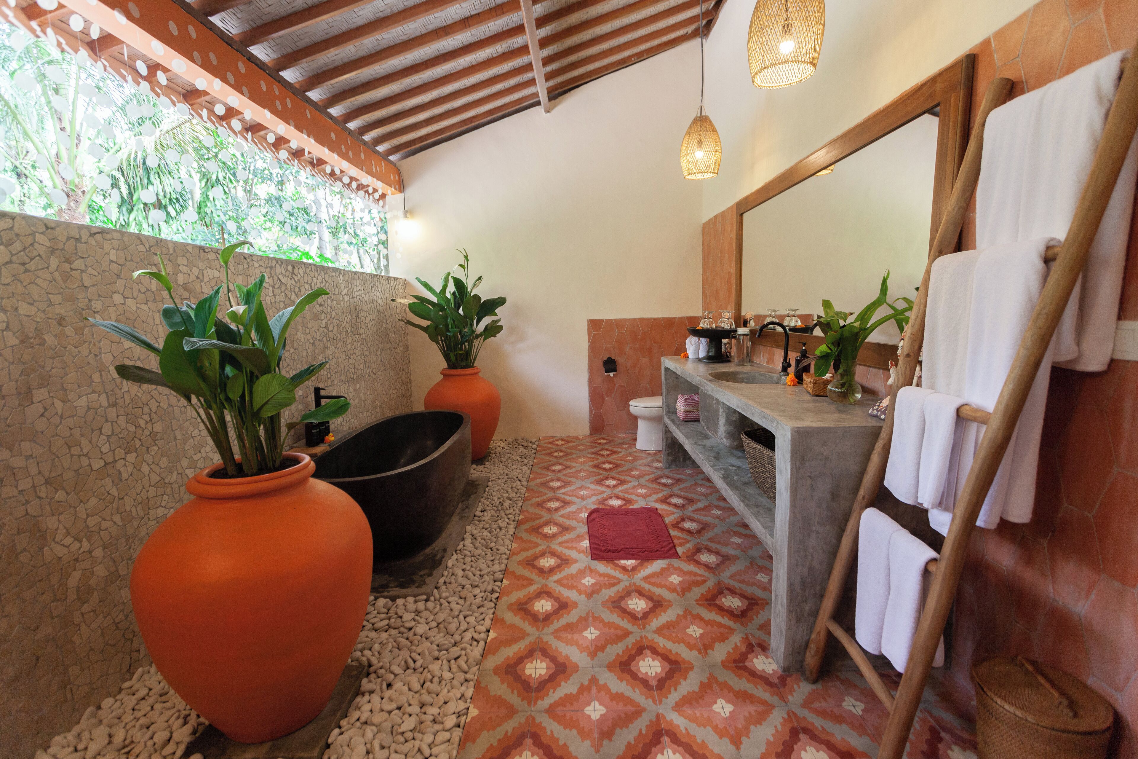 Un baño con una bañera grande, un lavabo con espejo y dos plantas en macetas.