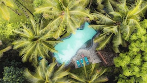 An aerial view of a tropical resort with a swimming pool surrounded by palm trees and a small beach area with lounge chairs. - Darmada Eco Resort (Sidemen)