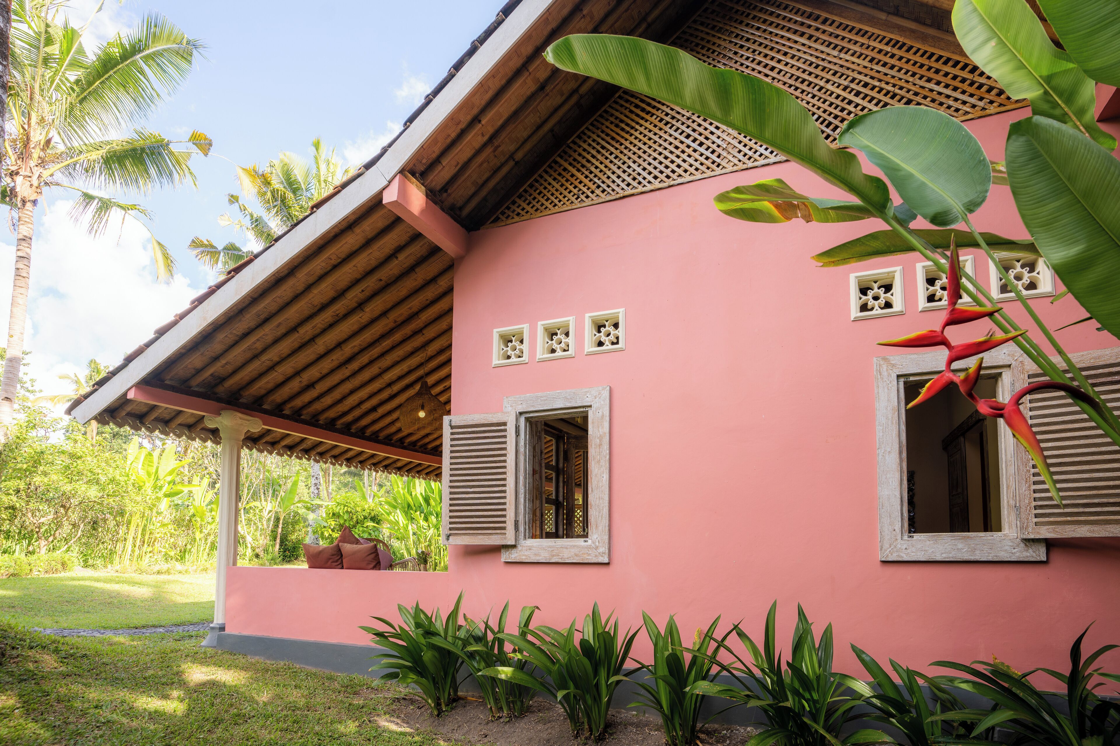 A pink building with wooden shutters, a covered porch, and tropical plants.