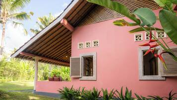 A pink building with wooden shutters, a covered porch, and tropical plants.