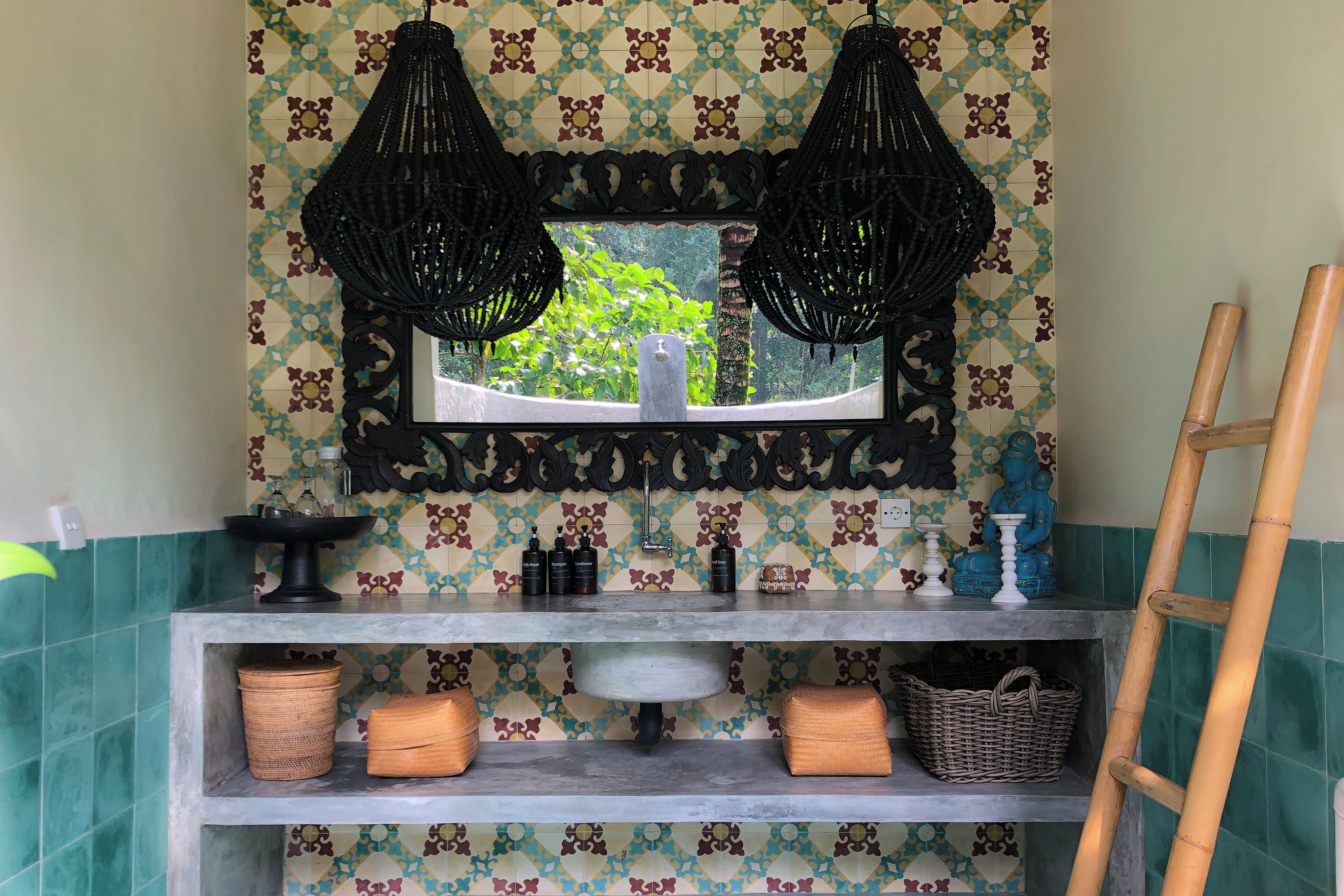 A bathroom with a decorative mirror, two black hanging lamps, a sink with toiletries, and a shelf with baskets.