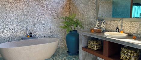 Un baño con una bañera independiente, un lavabo, un jarrón grande y un espejo.