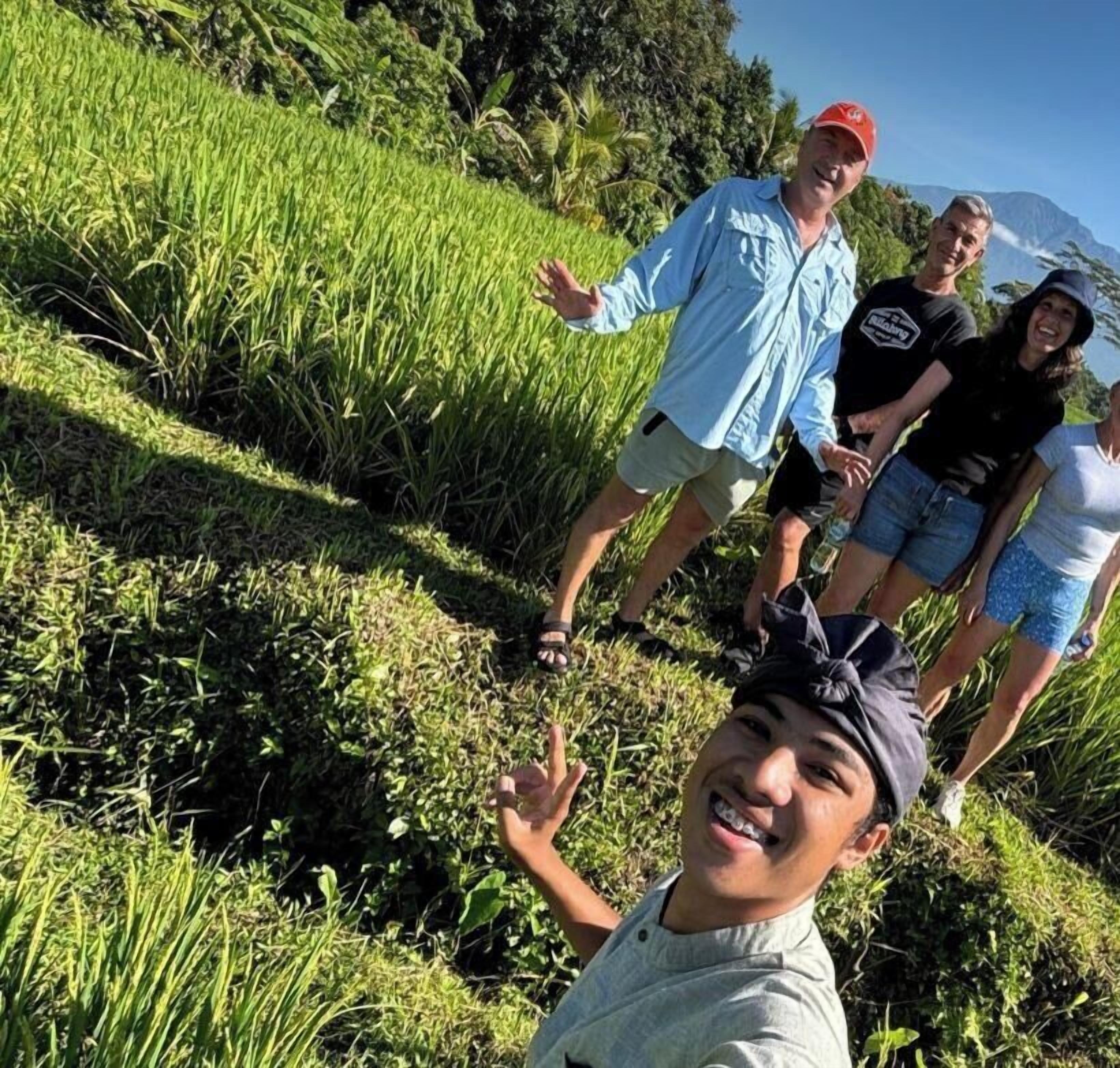 A group of people standing on a grassy slope with lush vegetation and a clear sky.
