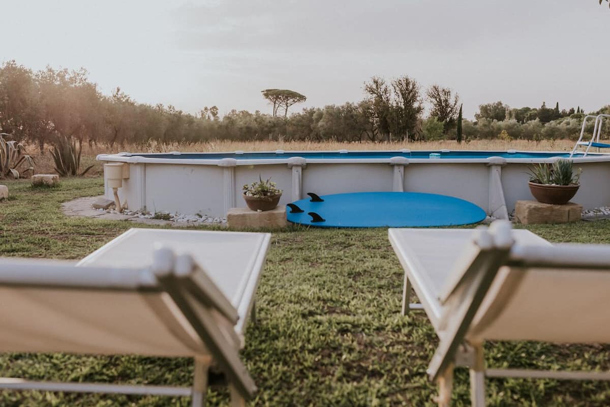 A swimming pool with two lounge chairs in the foreground, surrounded by a grassy area and potted plants.