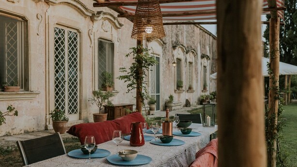 An outdoor dining area with a table set for two, surrounded by potted plants and a rustic pergola. - Villa Spada Donadeo (Lequile)