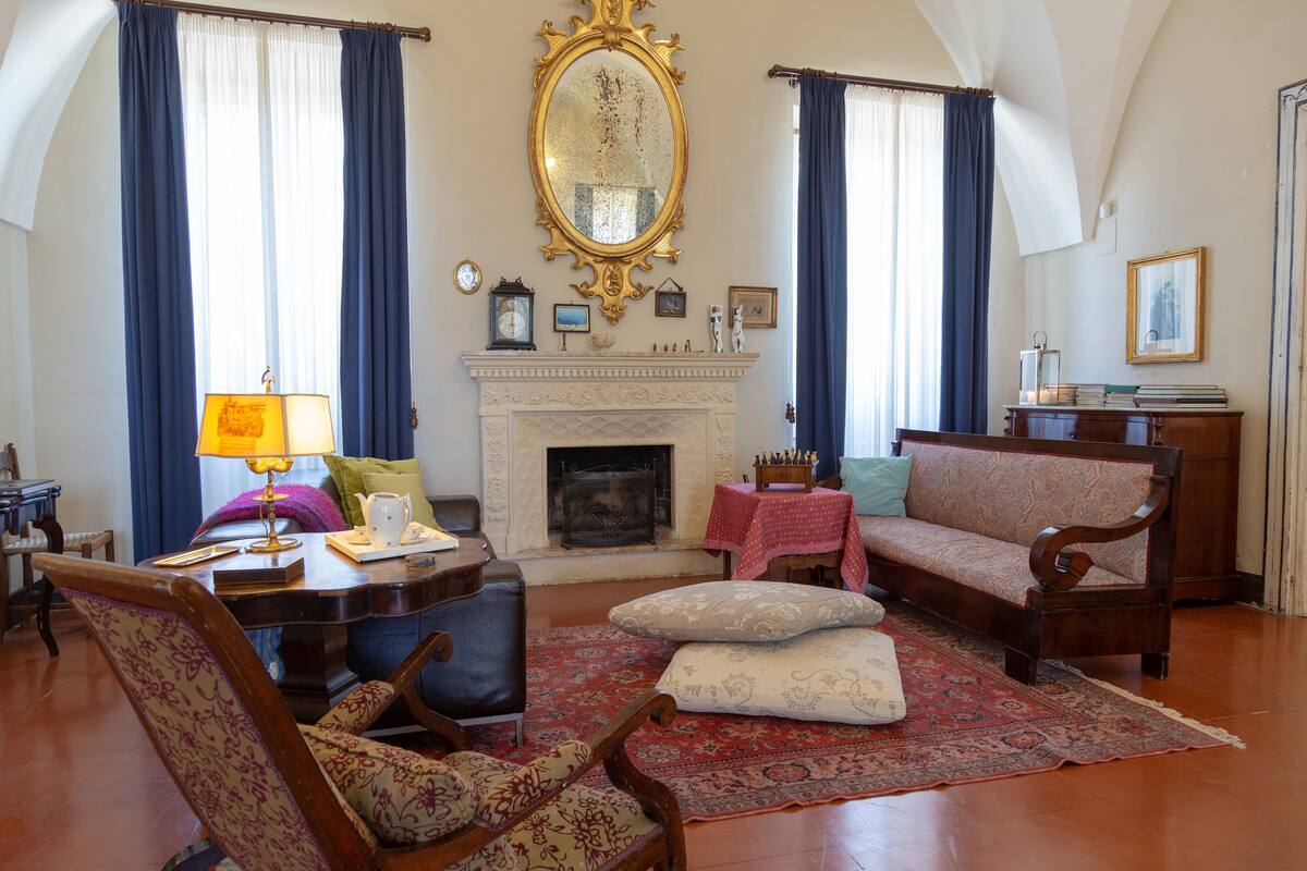 A traditional living room with a fireplace, a sofa, a table with a lamp, and a patterned rug.