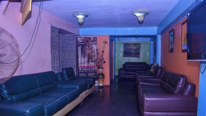 A reception area with a blue sofa, a brown sofa, a fan, and a poster advertising a beauty salon. - Duban International Hotels (Lagos)