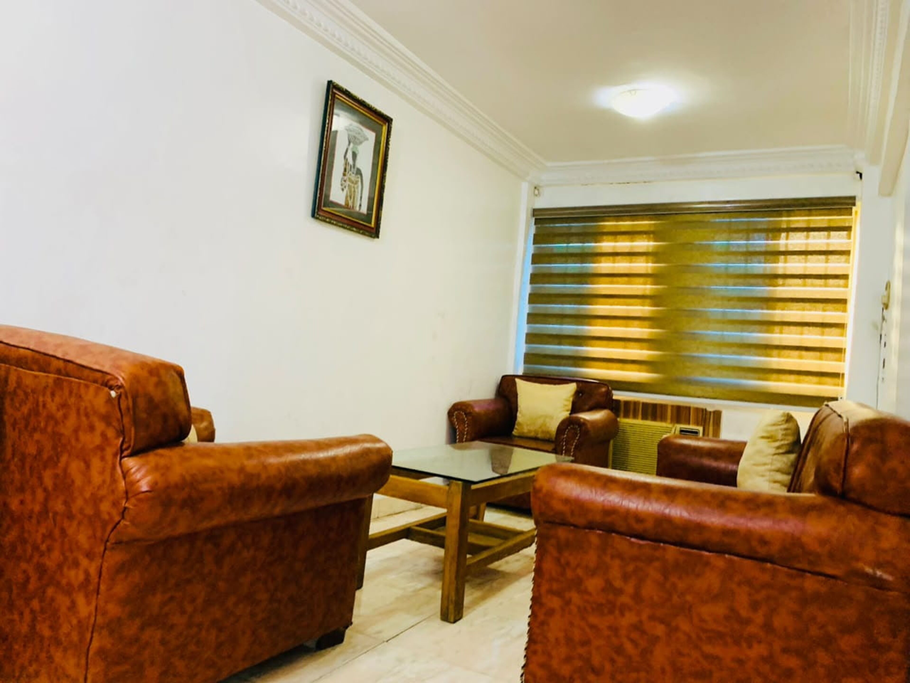 A living room with leather sofas, a glass coffee table, a framed picture on the wall, and a window with blinds.