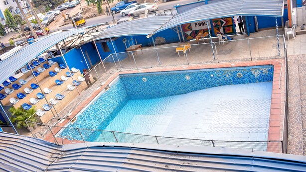 A swimming pool with blue tiles and a tiled deck area with chairs. - Duban International Hotels (Lagos)