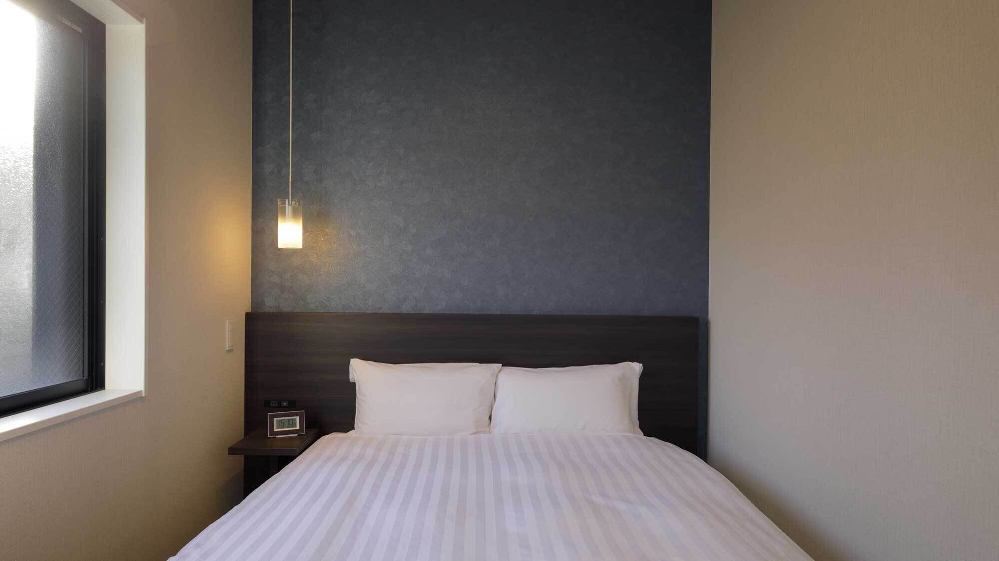 A hotel room with a bed, a nightstand, a wall clock, and a window.