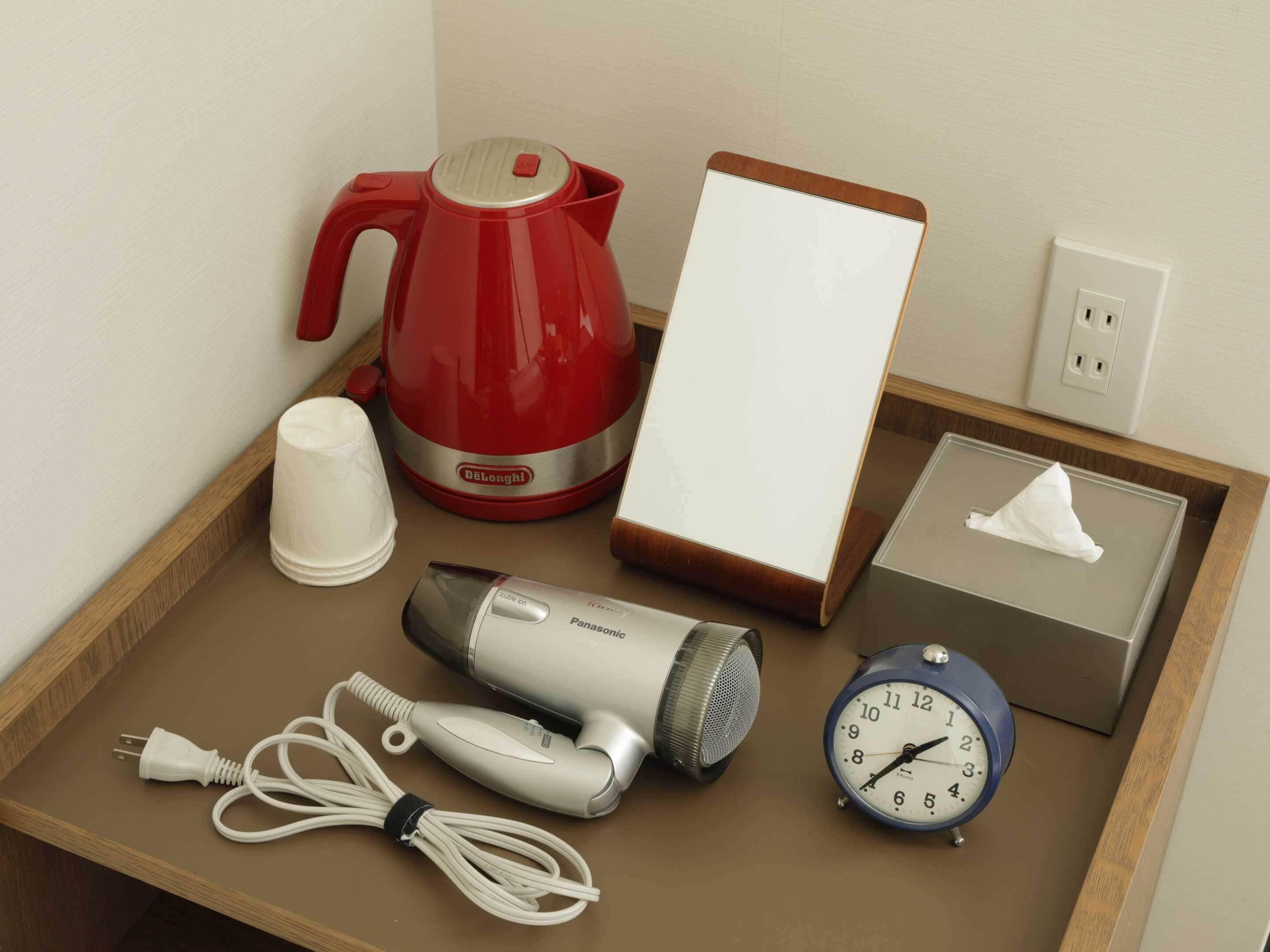 Un plateau avec une bouilloire rouge, une tasse blanche, un sèche-cheveux, une horloge et une boîte de mouchoirs.
