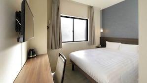 Habitación de hotel con cama, escritorio, silla, televisor, ventana con cortinas y mesita de noche.