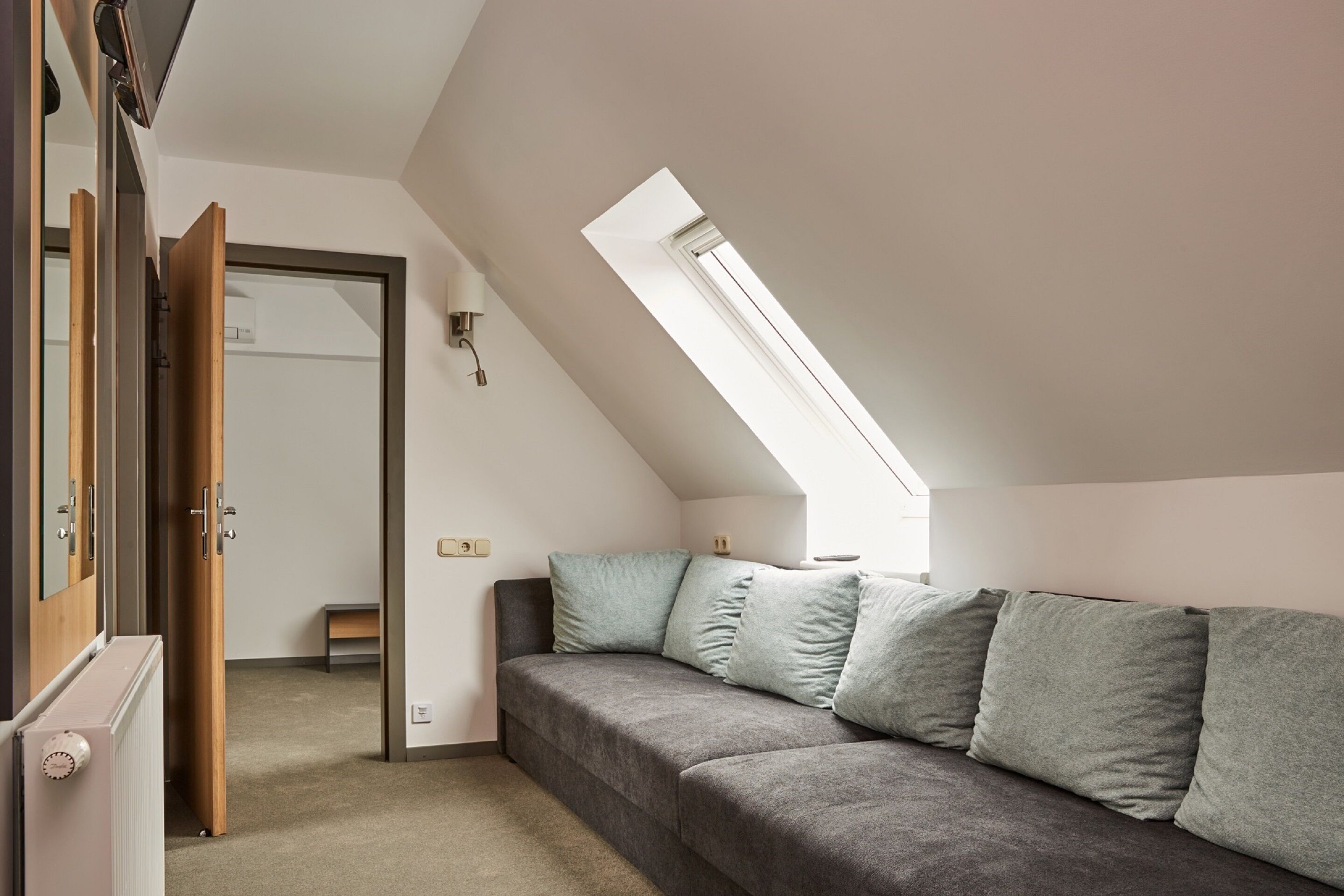 Een knus slaapkamer op zolder met een schuine plafond, een ingebouwde bank en een groot raam dat voor daglicht zorgt.