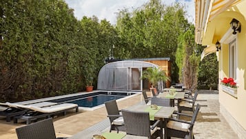 Un área junto a la piscina con sillas de descanso, un espacio de estar cubierto y una piscina.