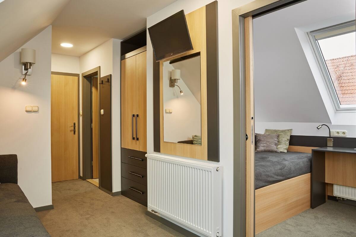 A bedroom with a sloped ceiling, a bed, a desk, and a window.