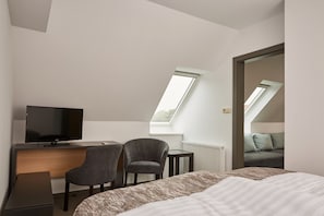 Une chambre d’hôtel moderne équipée d’un lit, d’un bureau avec une télévision, de deux chaises, d’une petite table et d’une lucarne.