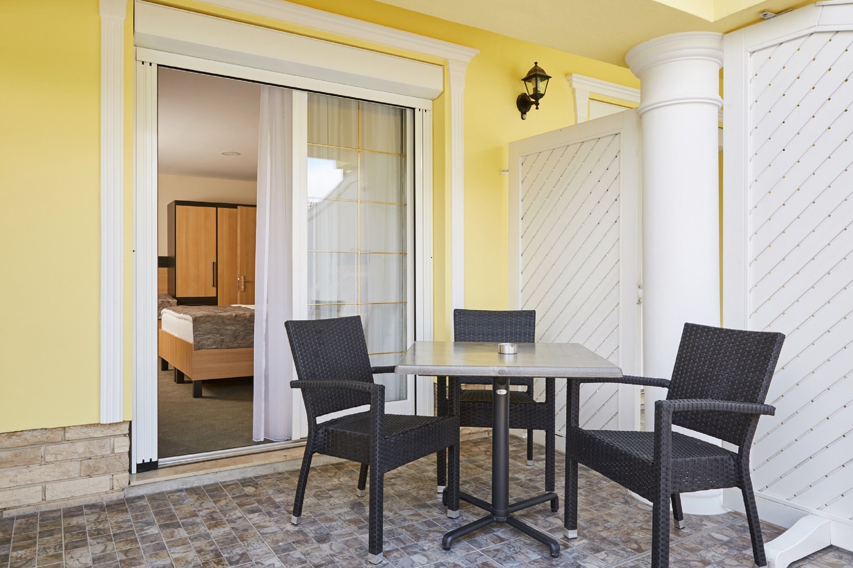 A room with a sliding glass door leading to a bedroom, a small table with two chairs, and a white column with a textured pattern.