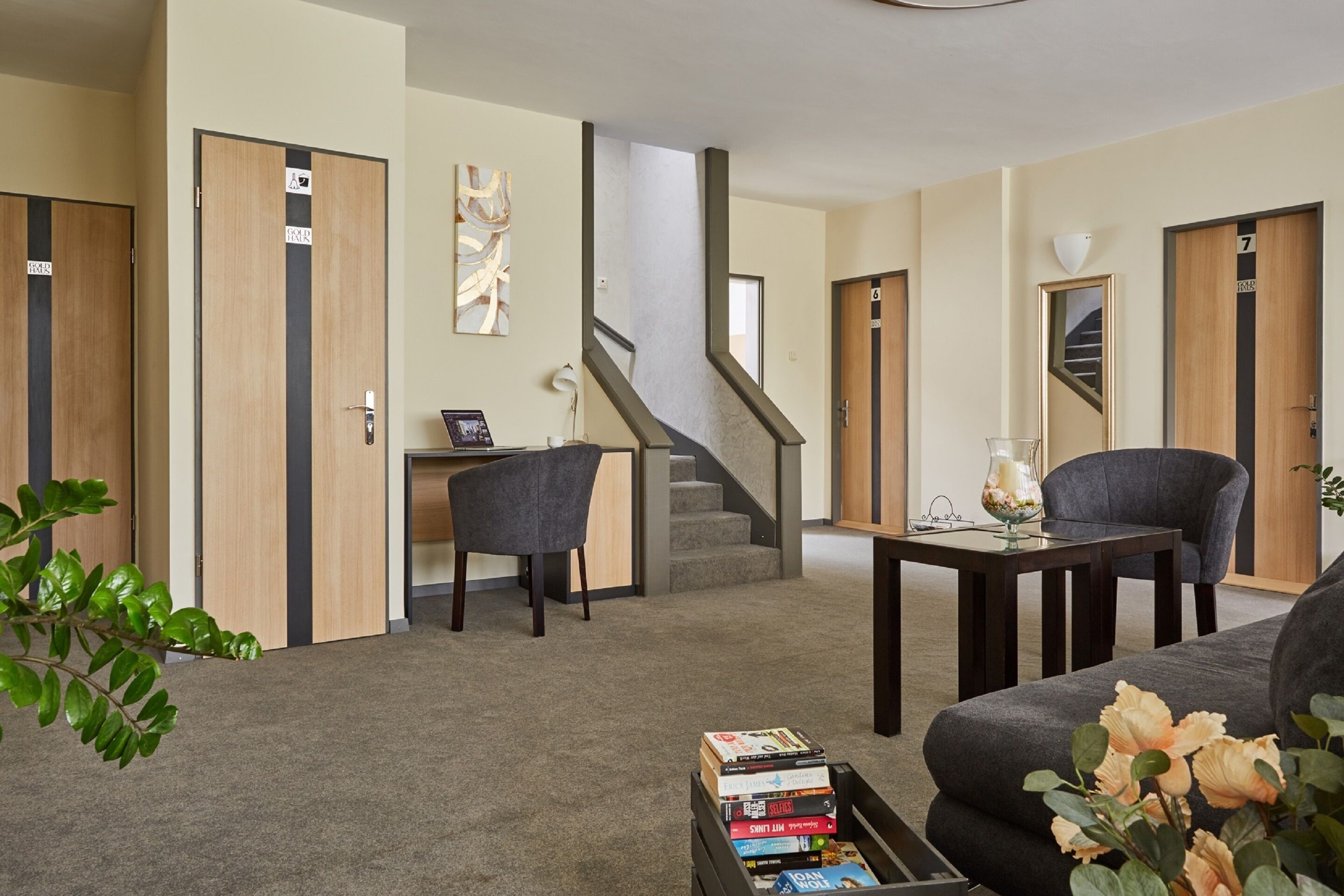 A modern living room with a sofa, a coffee table with books, a desk with a chair, and a staircase.