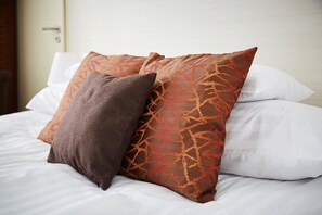 A bed with white bedding and two decorative pillows, one brown and one orange with a leaf pattern. - Astoria Hotel (Balatonfured)