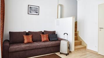 Une pièce meublée avec un canapé, une valise, un tableau encadré au mur et un escalier.