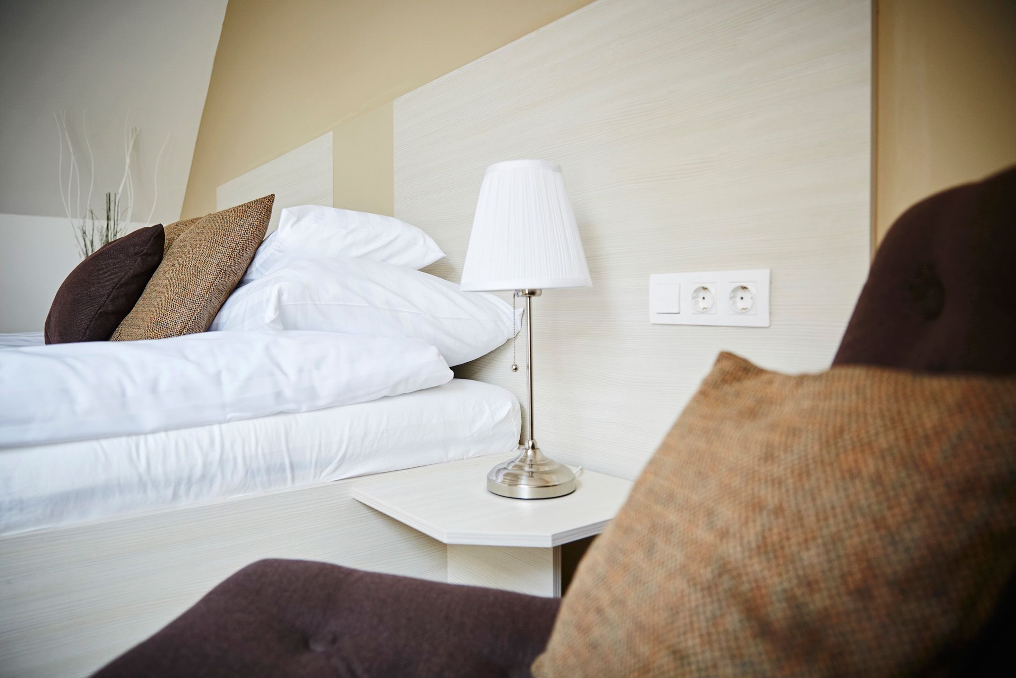 Una cama bien hecha con sábanas blancas y una lámpara moderna en una mesita de noche.