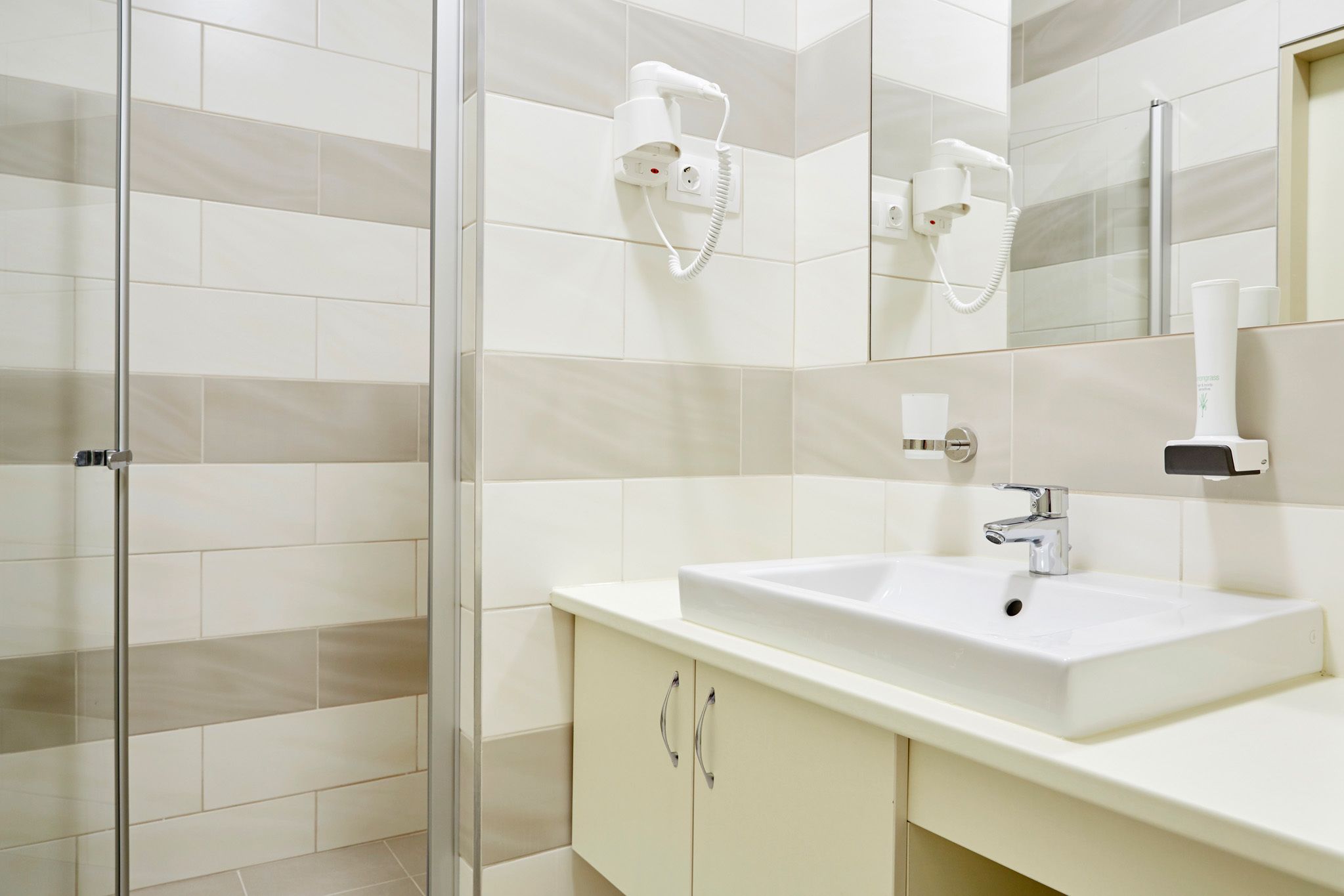 Un baño con un lavamanos blanco, cabina de ducha con paredes de vidrio y un espejo sobre el lavamanos.