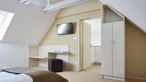 Une chambre à coucher comprenant un lit, un téléviseur fixé au mur, une armoire et un bureau avec une chaise.