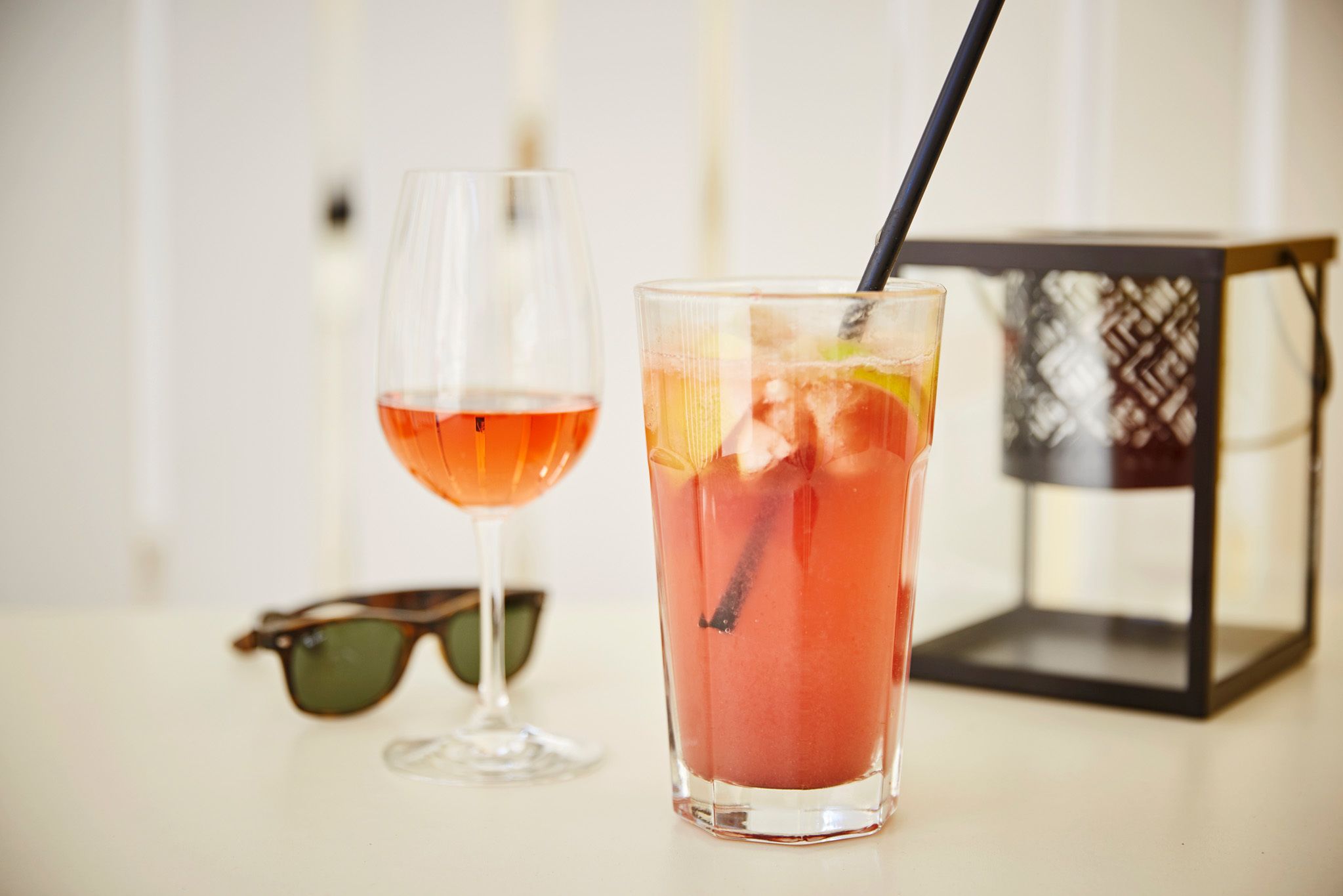 Two glasses of red beverage, one with a straw, and a pair of sunglasses on a table.