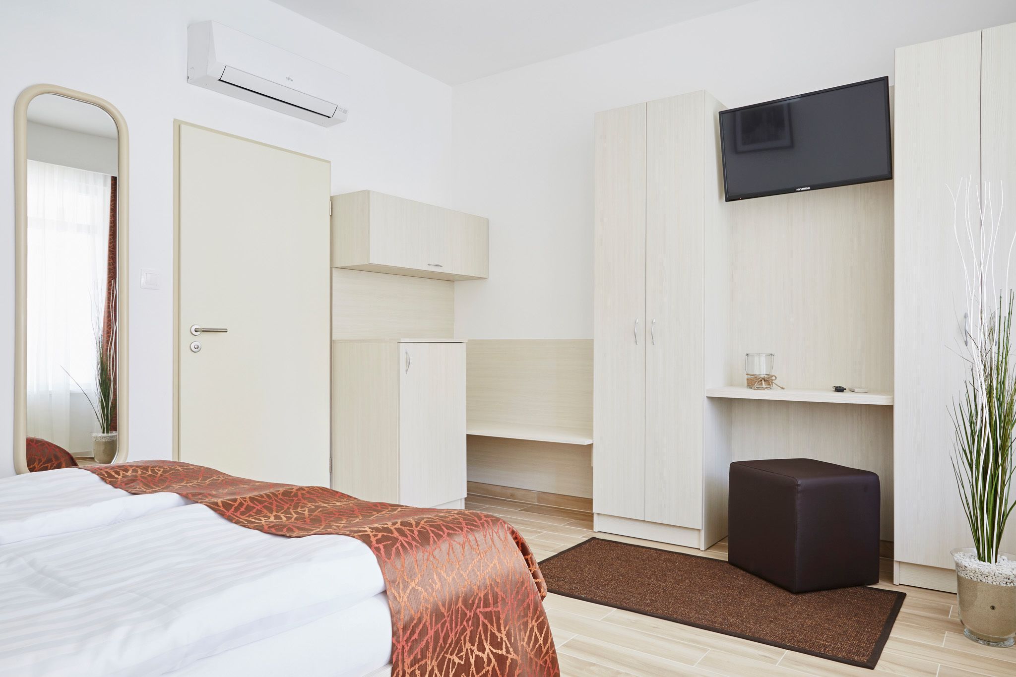 A hotel room with a bed, a wardrobe, a television, and a small potted plant.