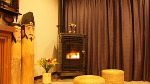 A cozy room with a wood-burning stove, a traditional Japanese screen, and two woven ottomans. - Oyado Uchidaya (Nozawaonsen)