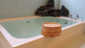 A bathtub with a wooden bucket, tiled walls, and a stone wall in the background. - Oyado Uchidaya (Nozawaonsen)