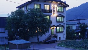 A two-story building with a balcony on the second floor, a car parked in front, and a tree in the foreground. - Oyado Uchidaya (Nozawaonsen)