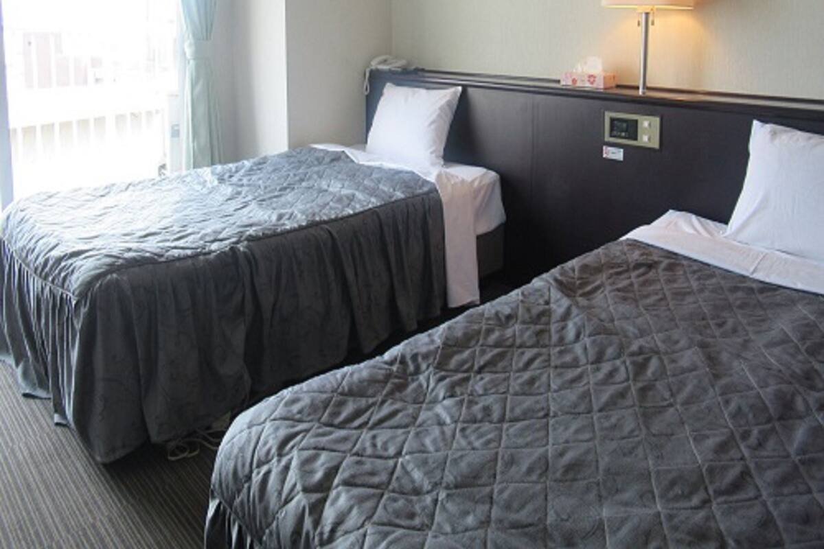 Une chambre d’hôtel avec deux lits, une fenêtre avec des rideaux, une lampe de chevet et une vue sur les bâtiments environnants.