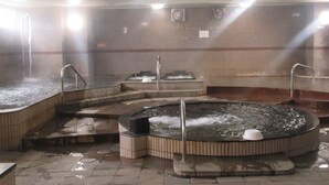 Un baño de vapor con varias bañeras de hidromasaje y una piscina central, rodeado de paredes de azulejos y un techo inclinado.