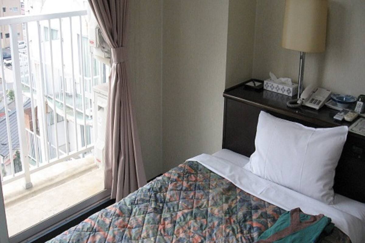 Une chambre d’hôtel avec un lit, une table de chevet avec une lampe, un téléphone et une fenêtre avec des rideaux.