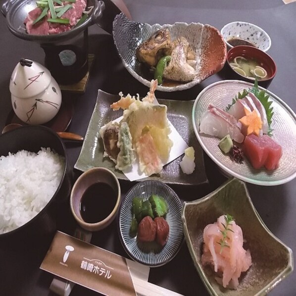 Variedad de platos japoneses, incluyendo sushi, sashimi y tempura, servidos en una mesa con palillos y cuencos.