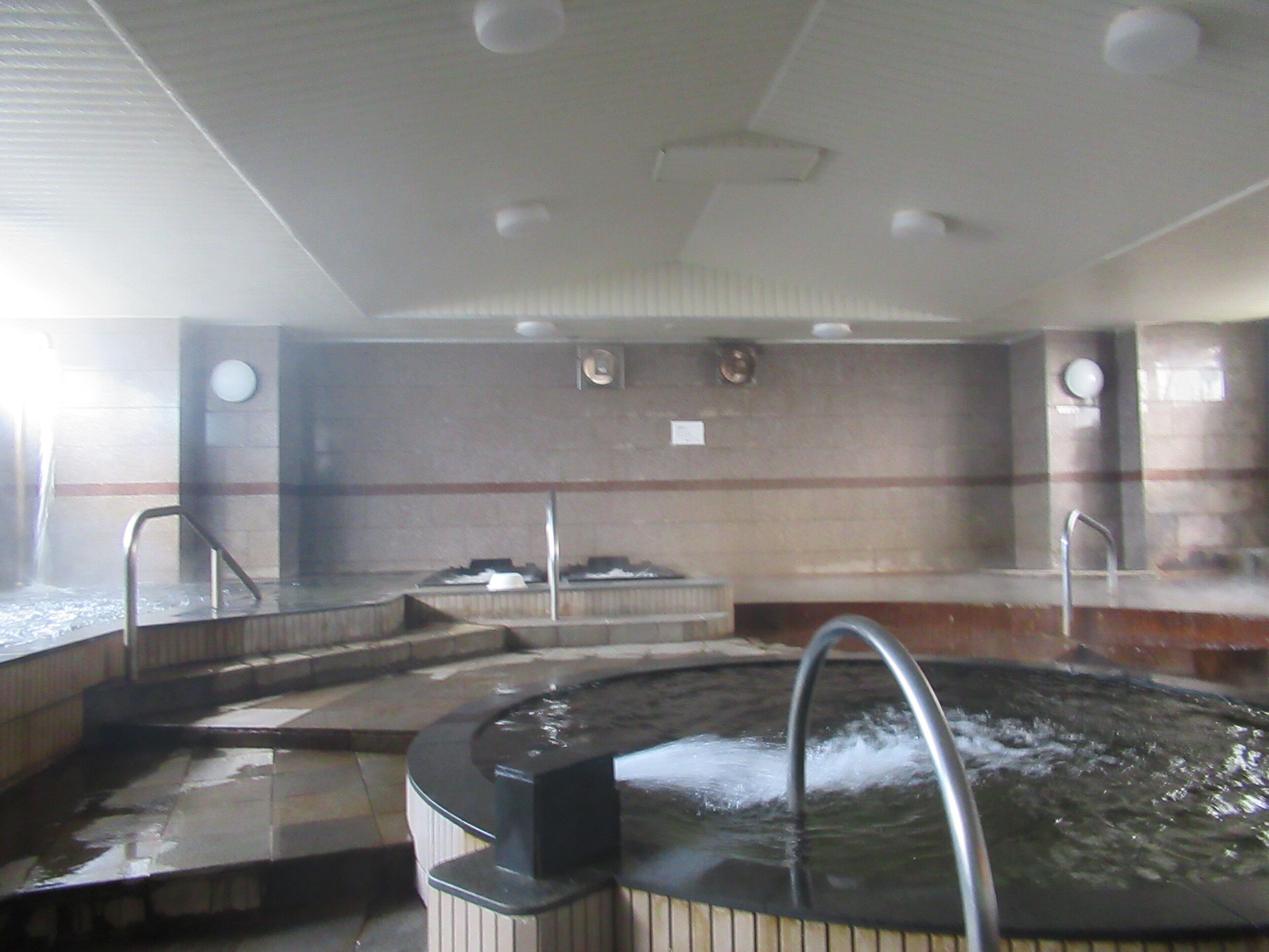 A hot tub area with steps leading into it, a wall-mounted heater, and a ceiling with recessed lighting.