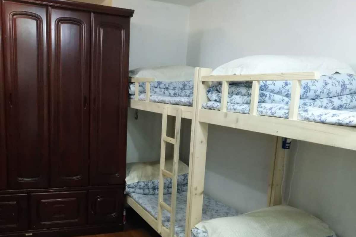 A room with two bunk beds, wooden wardrobe, and a wooden floor.