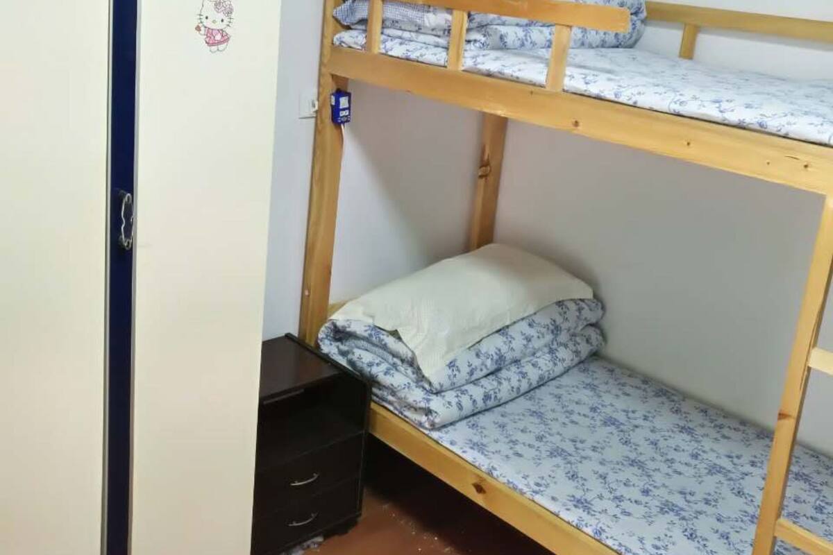 A bunk bed with a wooden frame and floral bedding, a wardrobe with a dark handle, and a small drawer unit.