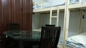 A room with a wooden cabinet, a glass-top table, two black chairs, and a bunk bed with a white mattress and blue patterned bedding. - Shanghai Yuelai Guest House - Hostel (Shanghai)