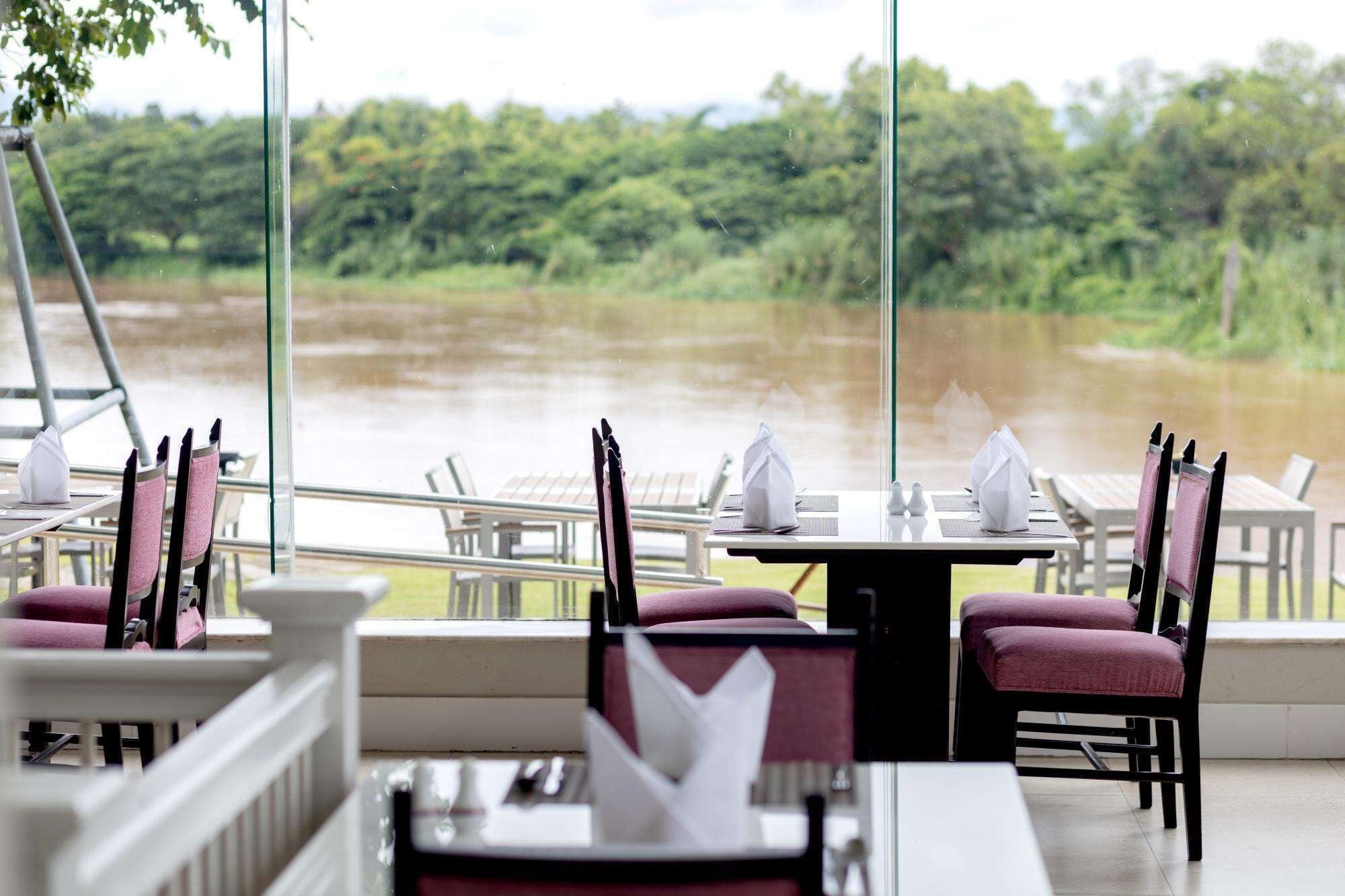 A restaurant with outdoor seating overlooking a river, featuring tables with chairs and neatly arranged napkins.