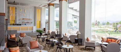 A spacious lobby with multiple seating areas, a bar, and large windows offering a view of the outdoors.