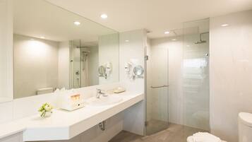 A modern bathroom with a large mirror, two sinks, a glass shower enclosure, and a toilet.