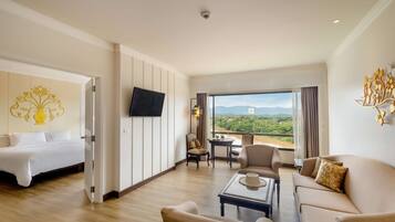 Una camera d'albergo con un letto, un divano, un tavolino, una televisione e un balcone con vista sulle montagne.