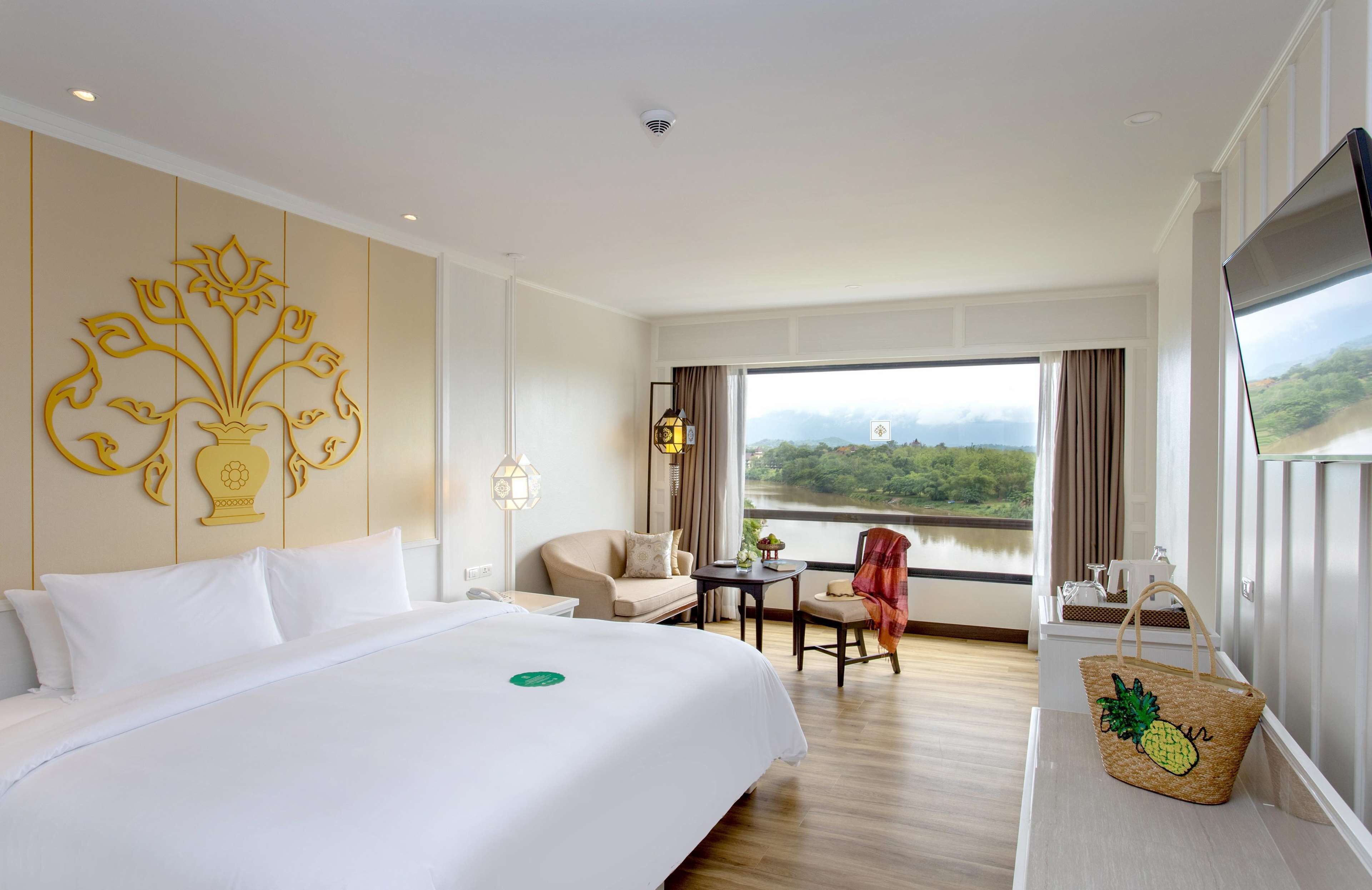 A hotel room with a large bed, a desk, a chair, and a view of a river.
